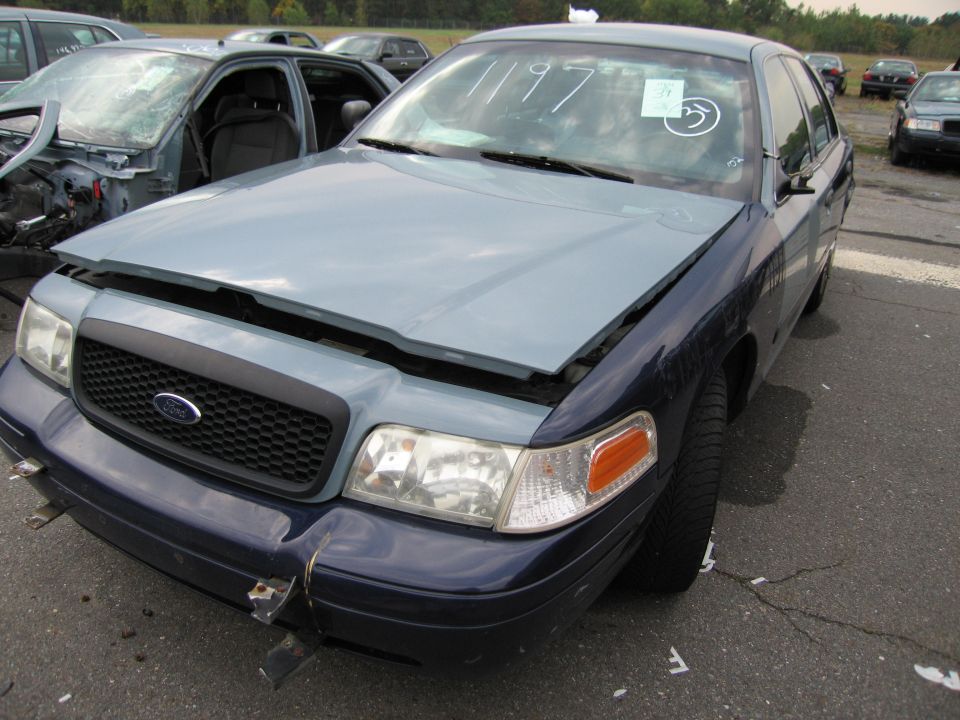 Ford Crown Victoria with hood open, showing a light blue hood and dark blue fenders. Another damaged car is visible to the left