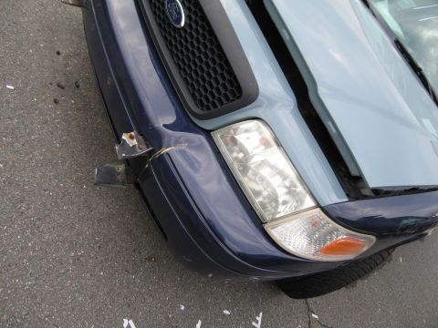 1991 Ford LTD Crown Victoria - The front end of a Ford Crown Victoria shows damage to the bumper and hood, with the hood slightly ajar.