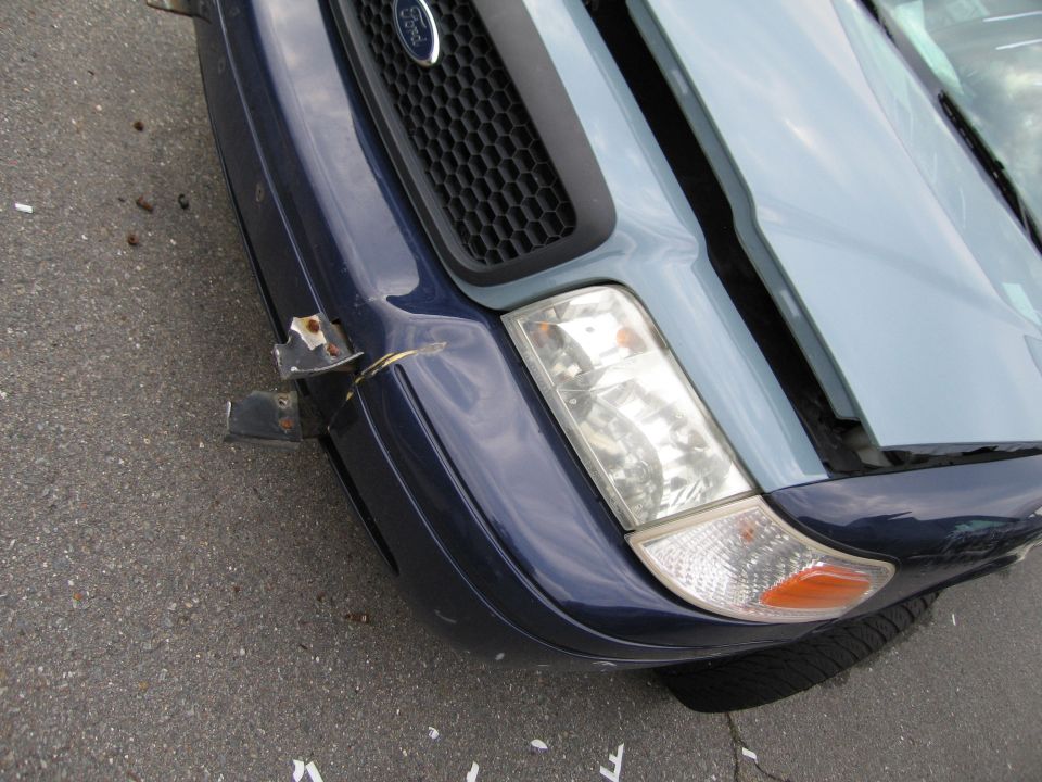 Front corner of a dark blue Ford Crown Victoria with a damaged bumper and hood