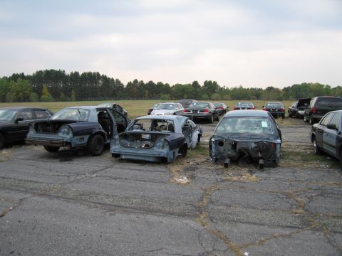 1991 Ford LTD Crown Victoria - Junkyard scene with multiple stripped-down vehicles, some with doors ajar and missing body panels.