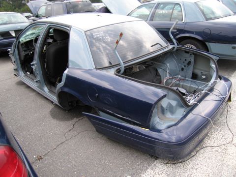 1991 Ford LTD Crown Victoria - Disassembled dark blue sedan with open trunk and visible interior components, parked among other vehicles.
