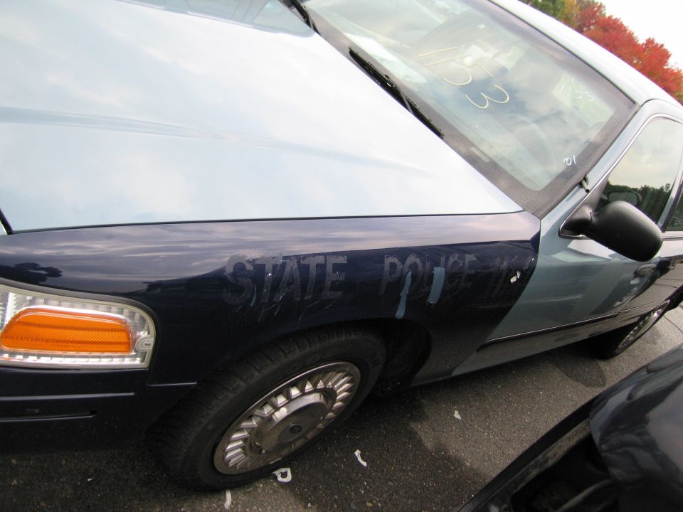 Police car fender with 'STATE POLICE' text. Another car is partially visible
