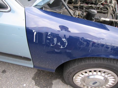 1991 Ford LTD Crown Victoria - Scratched text on a blue car fender, with the hood open revealing the engine.
