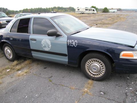 1991 Ford LTD Crown Victoria - A two-tone police car, possibly a 1992 model, is parked on cracked asphalt with a faded circular emblem on the door.