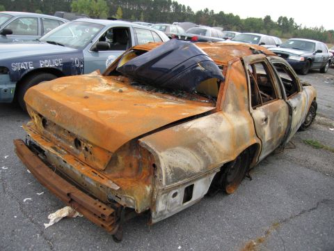 1991 Ford LTD Crown Victoria - A heavily damaged and burnt sedan sits in a vehicle lot, with other vehicles visible in the background.