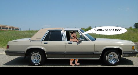 1988 Mercury Grand Marquis - A cartoon character appears to be driving a beige sedan, with a speech bubble saying 'YABBA DABBA DOO!'.