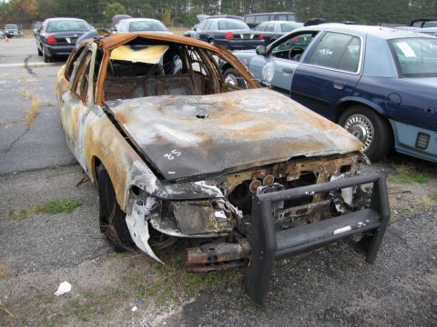 1991 Ford LTD Crown Victoria - A heavily damaged and burned car sits in an outdoor lot next to other vehicles.
