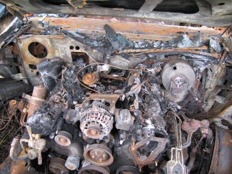1991 Ford LTD Crown Victoria - The engine compartment of a vehicle is heavily damaged by fire, with charred remains and corroded parts visible.