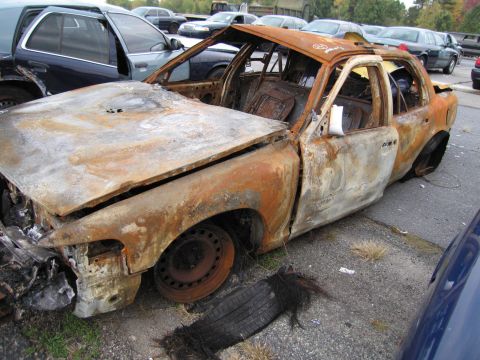 1991 Ford LTD Crown Victoria - A severely damaged and burnt sedan sits in a lot, showing extensive fire damage.