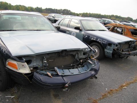 1991 Ford LTD Crown Victoria - Several damaged vehicles, including two police cruisers, are parked in an outdoor lot.