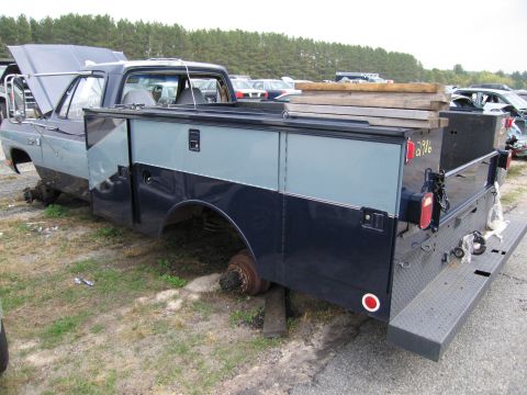 1991 Ford LTD Crown Victoria - A two-tone pickup truck with a utility bed sits in a junkyard, missing its wheels.