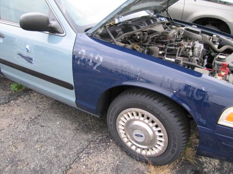 1991 Ford LTD Crown Victoria - The front passenger side of a two-tone Ford Crown Victoria is shown with the hood up, revealing the engine compartment.