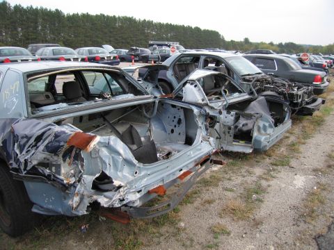 1991 Ford LTD Crown Victoria - Multiple heavily damaged police vehicles are parked in a lot, awaiting salvage or disposal.