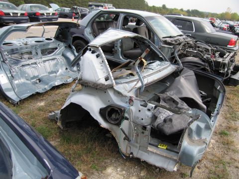 1991 Ford LTD Crown Victoria - Disassembled car chassis in a junkyard, with other vehicles visible in the background.