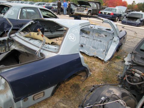 1991 Ford LTD Crown Victoria - This car chassis, stripped of most components, sits in a junkyard with other vehicles visible in the background.
