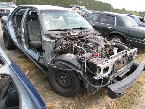 1991 Ford LTD Crown Victoria - This heavily damaged Ford Crown Victoria is missing its front bumper and doors, with the engine compartment exposed.