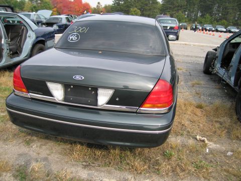 1991 Ford LTD Crown Victoria - A dark green Ford Crown Victoria sits in a junkyard with other vehicles.