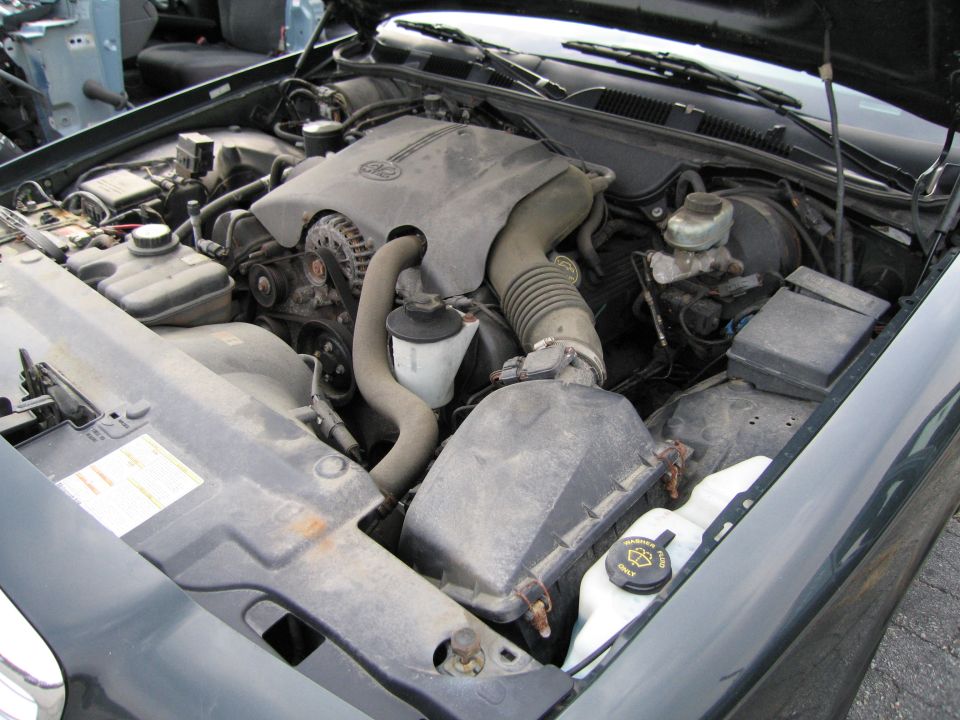 Engine bay of a dark green car, showing the engine, air intake, and various fluid reservoirs