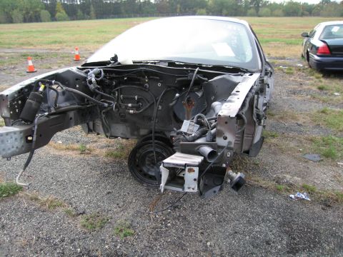 1991 Ford LTD Crown Victoria - A car's front end is dismantled, revealing the engine bay and chassis. Another vehicle sits nearby in a grassy lot.