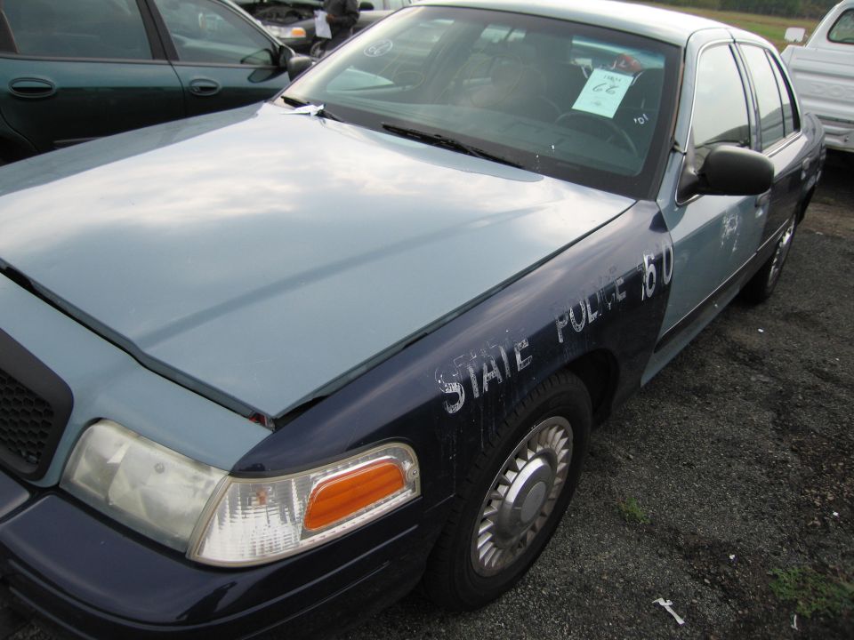Ford Crown Victoria police car with 'STATE POLICE 150' on fender. Another car is parked next to it