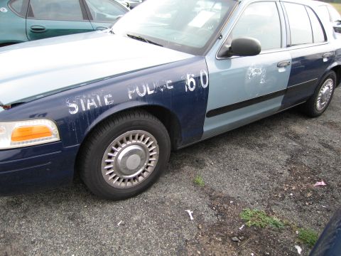 1991 Ford LTD Crown Victoria - A two-tone police car with "STATE POLICE 60" visible on its side is parked on a gravel lot.