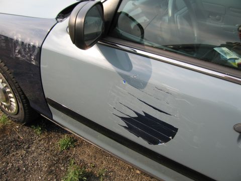 1991 Ford LTD Crown Victoria - A light blue car door shows significant damage and a large repair patch made of black tape.