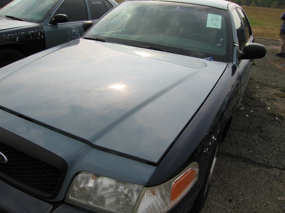 Blue Ford Crown Victoria with a sticker on the windshield, parked next to another car