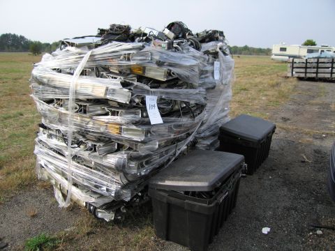 1991 Ford LTD Crown Victoria - A large pallet containing numerous car headlights and associated wiring, secured with plastic wrap, sits outdoors next to two black storage…