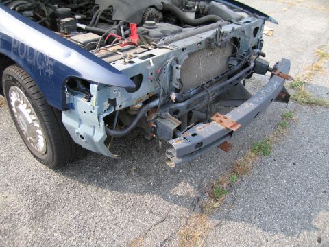 1991 Ford LTD Crown Victoria - Front end of a damaged blue police car, showing the grille and engine components. The "POLICE" text is visible on the fender.