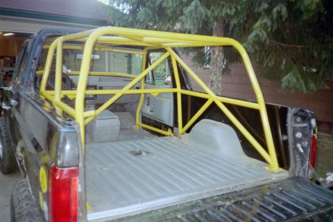 1988 Ford Bronco - Rear view of a black pickup truck modified with a prominent yellow roll cage.