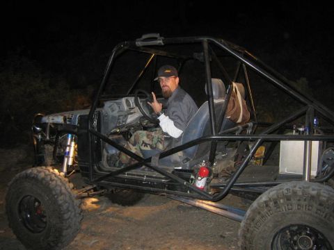 1994 Ford Bronco - Man sits in a custom off-road buggy with a prominent roll cage and large tires.