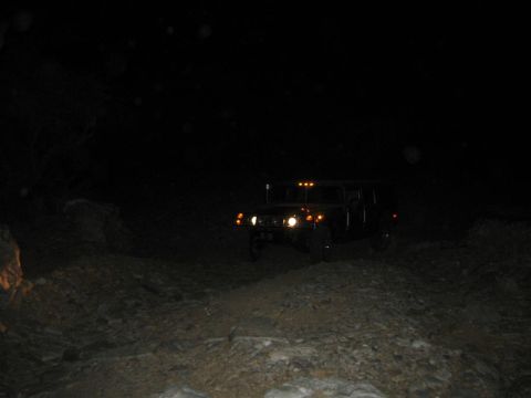 1994 Ford Bronco - A Hummer H1 navigates a rough terrain in the dark, its headlights cutting through the night.