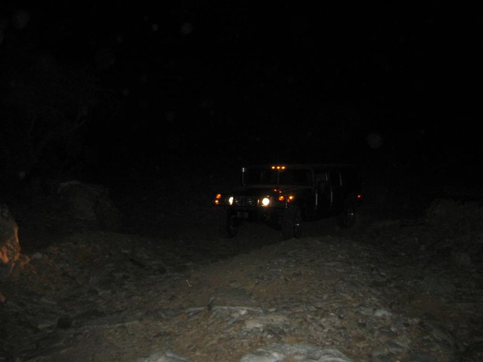Dark Hummer H1 driving on a dirt road at night, headlights on