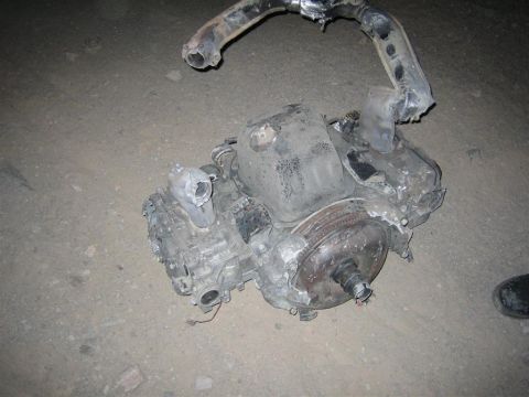1994 Ford Bronco - A damaged engine and transmission assembly lies on the ground, its exhaust pipe bent and broken.