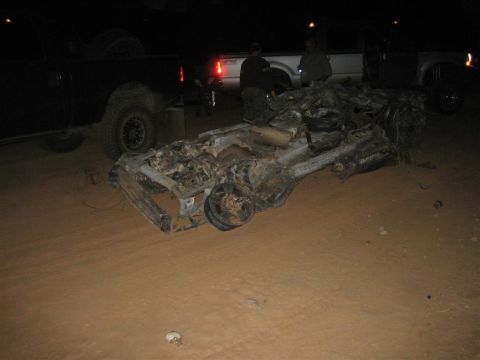 1994 Ford Bronco - The heavily damaged chassis of a vehicle lies on the ground at night, with other vehicles visible in the background.