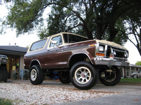 1979 Ford Bronco - A lifted 1979 Ford Bronco with a two-tone paint job sits outside a garage.