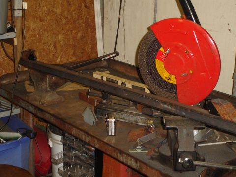 1989 Ford Bronco - A chop saw is used to cut a metal bar that is secured in a vise on a workbench.