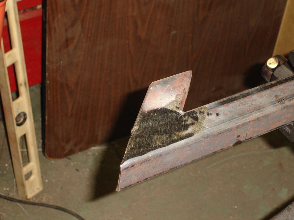Close-up of a metal bracket with rough edges, next to a level and a wooden board