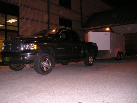 1989 Ford Bronco - Night shot of a dark Dodge Ram 2500 quad-cab pickup with a green John Deere front plate, parked on pavement outside a brick building while…