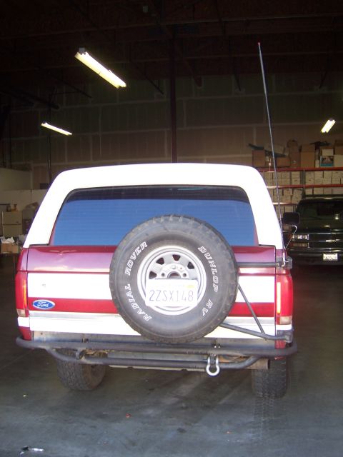 1991 Ford Bronco - Rear view of a red and white Ford Bronco with a spare tire on the back, parked indoors.