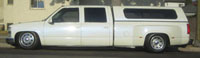 1968 Ford Mustang - A white dually pickup truck with a camper shell is parked on the street, showing its side profile.