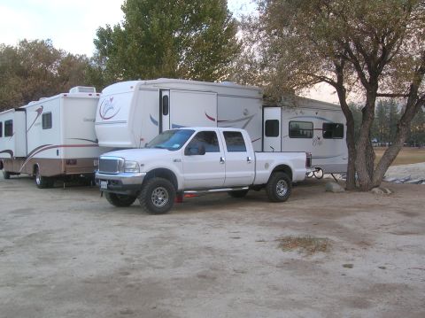 1985 Ford Bronco - A white Ford F-250 Super Duty pickup truck is parked in front of two large RVs at a campsite.