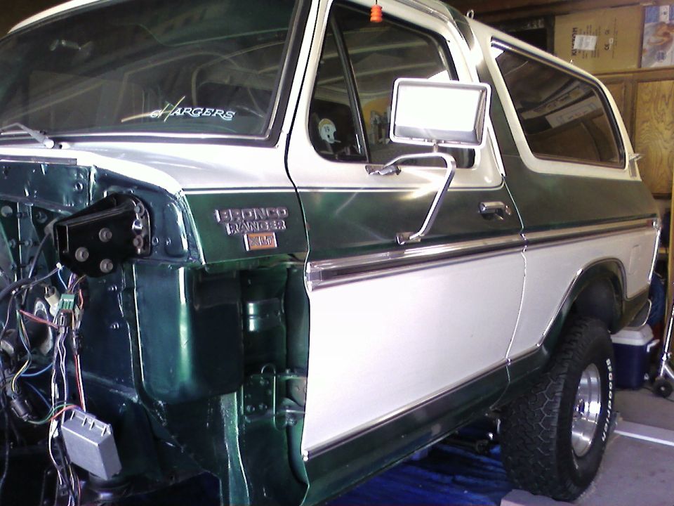 Green and white Ford Bronco SUV, driver side, in garage with front end partly disassembled