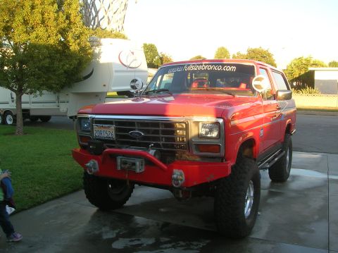 1985 Ford Bronco - This red 1985 Ford Bronco features a custom front bumper and winch, with a website address visible on the windshield.