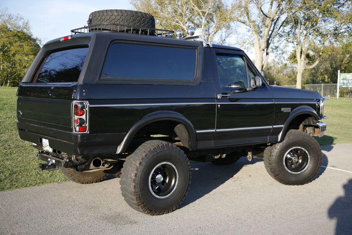 Black lifted Ford Bronco SUV, rear 3/4 view with big tires and roof rack spare