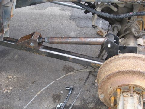 1990 Ford F-250 - This photo shows a custom steering linkage modification on a vehicle's rear axle assembly, with a rusty drum brake in view.