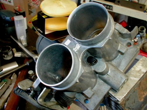 1996 Ford Bronco - A dual throttle body is shown on a workbench, surrounded by various tools and automotive parts.