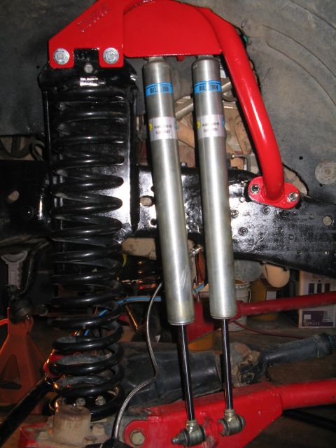 1989 Ford Bronco - Close-up of a vehicle's front suspension system, dual Bilstein shock absorbers and bright red control arms.