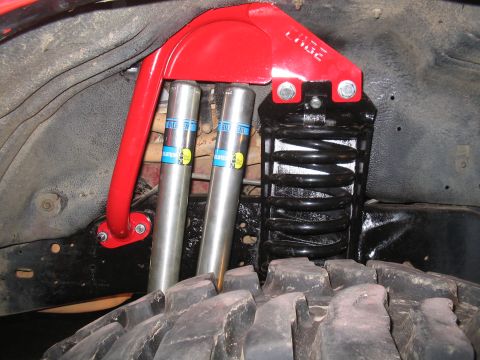 1989 Ford Bronco - Custom suspension components, including Bilstein shocks and a red brace, are visible near a large off-road tire.