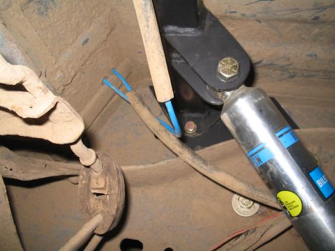 1989 Ford Bronco - Close-up view of a vehicle's undercarriage, focusing on the shock absorber mounting hardware and associated wiring.